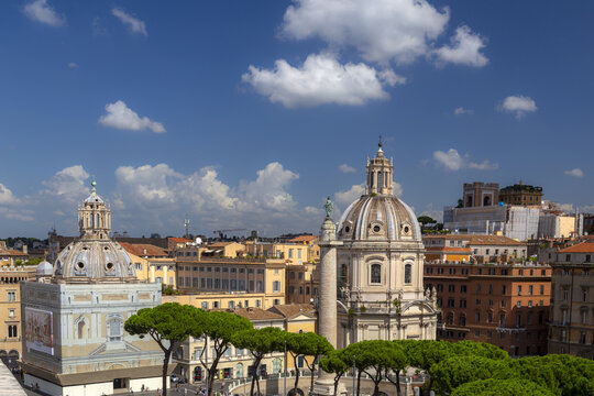 View of the Church of Santa Maria di Loreto and Trajan's Column surrounded by historic buildings and pine trees under a blue sky in Rome, Lazio, Italy.