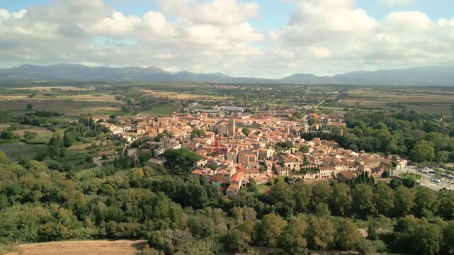 Aerial view of the historic town of Peralada surrounded by lush green trees and fields under a cloudy sky in Peralada, Catalonia, Spain.