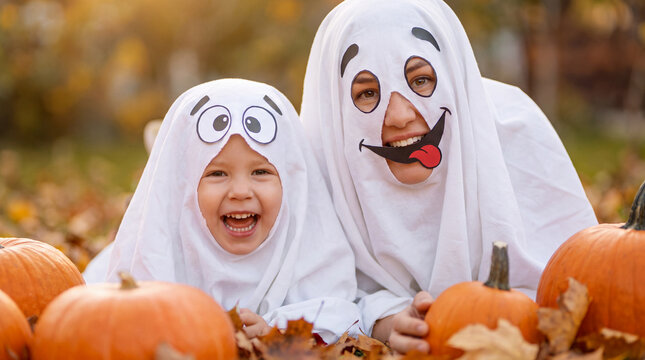 Laughing mother and daughter in cute ghost costumes making silly faces at camera for Halloween, ideal for festive family social posts and party banners.
