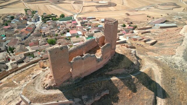 Aerial view of a ruined stone castle on a hill overlooking a small village with terracotta rooftops in Spain.