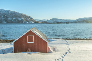 Red wooden cabin by a snowy fjord in Uløya, Troms County, Norway © Elsworth Frobisher