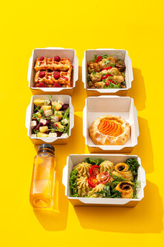 Daily healthy food delivery ration with waffles meat salad pastry and juice in containers on yellow background