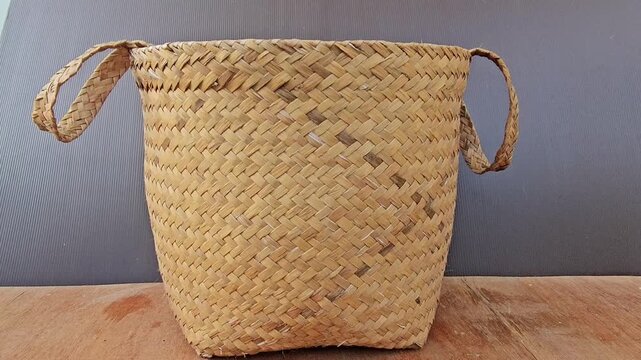 wicker basket on wooden background,Handwoven basket rests on wooden surface. Natural fibers form rustic, textured pattern. Four handles looped for easy carrying. Soft golden tones match warm wood