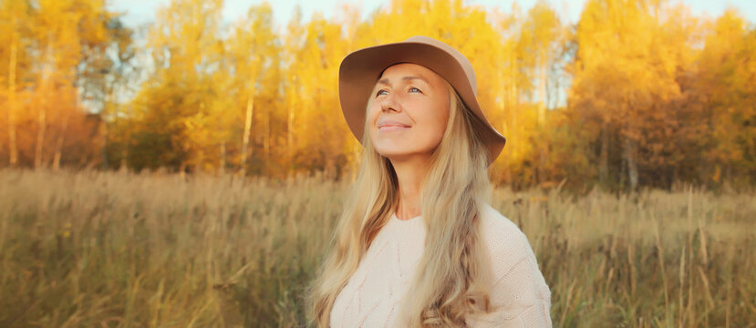 Happy smiling woman enjoying warm sunny weather in autumn park outdoors