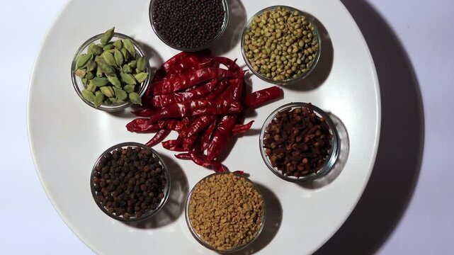 Set of dried Indian spices in serving plate and glass bowl table top view spin.