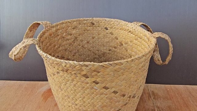 empty basket on wooden background,Handwoven basket rests on wooden surface. Natural fibers form rustic, textured pattern. Four handles looped for easy carrying. Soft golden tones match warm wood grain