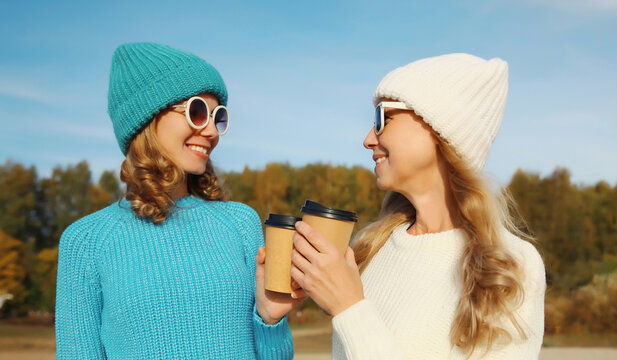 Happy young women friends talking with coffee drinks on beach, smiling girlfriends together on sea