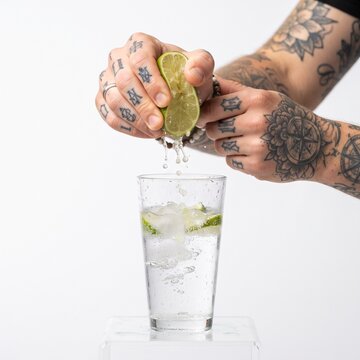 Man's tattooed hands squeezing lime into glass of water with ice
