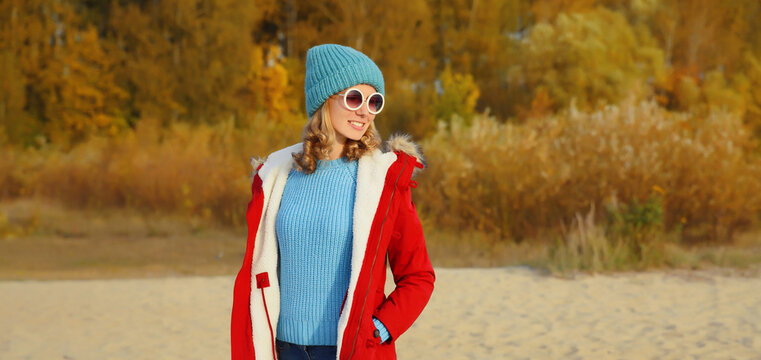 Modern stylish woman standing on beach looking away against autumn trees background