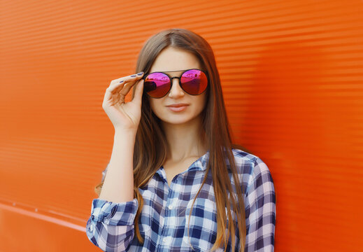 Portrait of modern stylish young woman in glasses, casual clothing posing on orange background