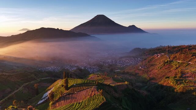 Aerial view of Sikapuk Hill and terraced fields at sunrise with Mount Prau in the background in Indonesia.