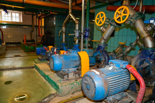 Large blue industrial motors drive metal pipes and yellow valves to circulate liquid pulp through a paper recycling facility interior