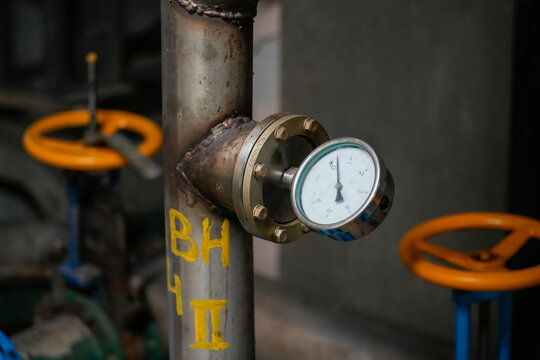 Metal pipe with a pressure gauge installed at a cardboard recycling plant shows system status during active daytime industrial operations
