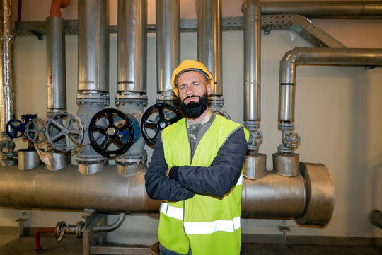 Professional technician with a beard stands before metal pipes at a recycling plant facility during his shift to inspect machinery and monitor operations