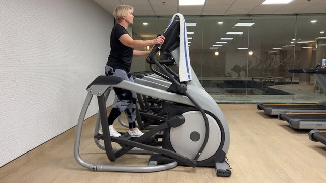A person uses an elliptical machine while focused on their workout in a gym setting. The gym has several equipment in view.