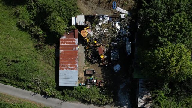Aerial view of industrial scrapyard with yellow excavators and piles of scrap metal next to a rusty building in Lancaster, England, United Kingdom.