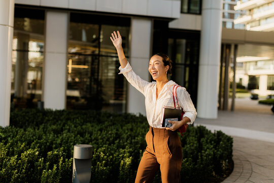 Korean woman joyfully waves while strolling through a modern urban landscape