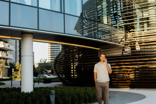 Man walking outside modern building while talking on phone during afternoon