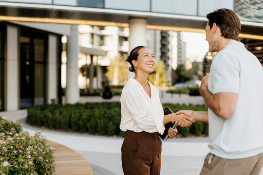 Korean woman and Caucasian man share a friendly handshake outdoors