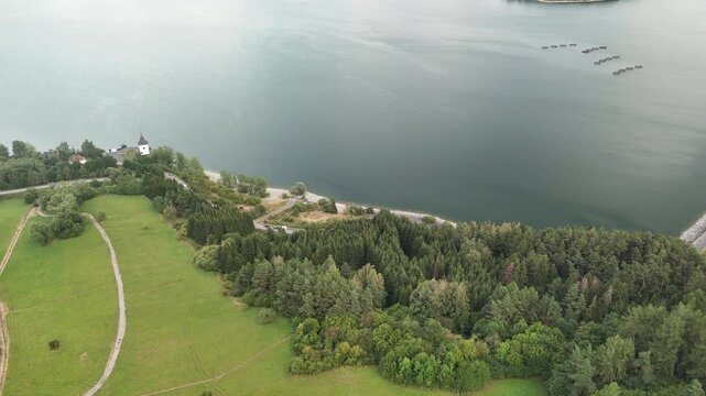 Aerial view of the Liptovska Mara reservoir featuring the historic church tower, surrounding green meadows, and dense forests in Liptovsky Mikulas District, Zilina Region, Slovakia.