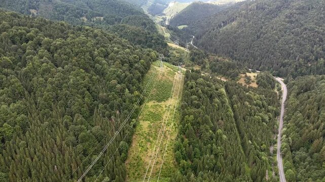 Aerial view of Korytnicka dolina valley with power lines cutting through dense forest and a winding road in Liptovska Osada, Zilinsky kraj, Slovakia.