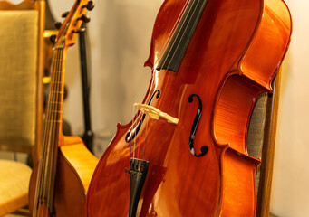 Classical cello and viola da gamba resting against chairs in a music studio. Close-up on the elegant wooden body, f-holes, and strings of stringed orchestral instruments in warm light. © Stanislav
