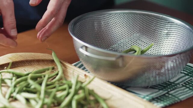 Person rinsing raw organic green beans in a colander, kitchen interior