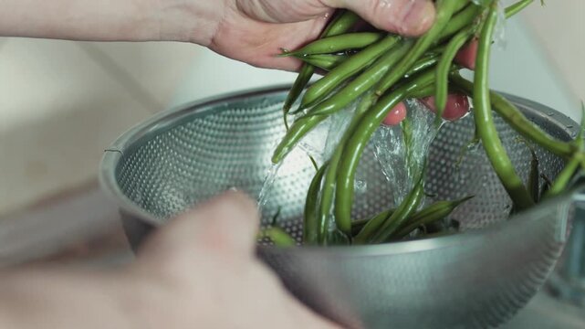 High angle shot of wet green beans inside a stainless steel strainer bowl