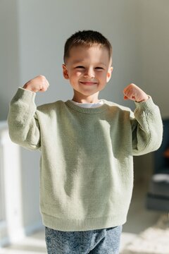 Young smiling boy flexing arms in green sweater at home for child portrait background and family banner