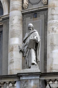 View of a marble statue of a bearded man holding a book and a palm frond, positioned in a niche between classical columns at the Uffizi Galleries in Firenze, Toscana, Italy.