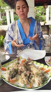 Woman presenting fresh cooked fish dish and salad at outdoor restaurant during travel