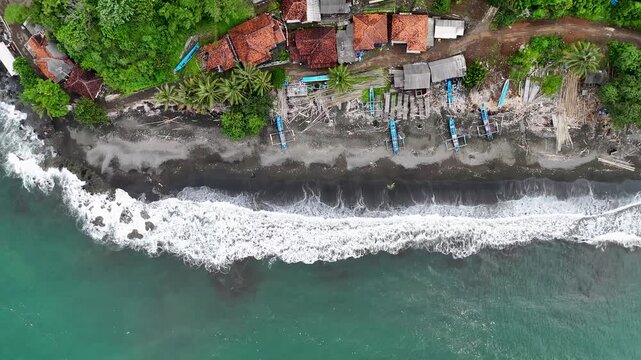 Aerial view of Ciletuh Geopark beach with traditional fishing boats on black sand, lush greenery, and coastal houses in Sukabumi, West Java, Indonesia.