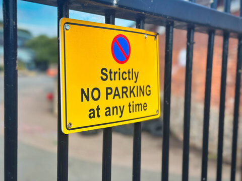 Strictly No Parking At Any Time Yellow Warning Sign on Metal Gate