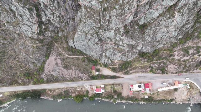 Cinematic top-down aerial footage of a steep rocky cliff and winding mountain road in the Sacred Valley of Peru.