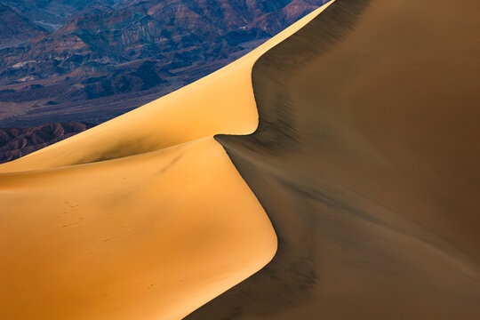 View of the sweeping sand dunes of Death Valley National Park with dramatic light and shadow contrast against the rugged mountain backdrop in Inyo County, California, United States.