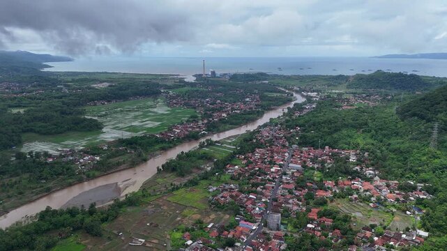Aerial view of Lio citarik river flowing through lush green landscape and village houses towards the coast in Kecamatan Pelabuhanratu, Jawa Barat, Indonesia.