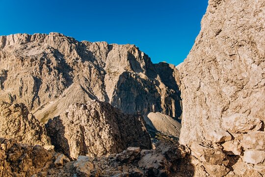 Jagged limestone Dolomite peaks rise against a deep blue sky beside a rocky pinnacle. Dramatic mountain wilderness for hiking, adventure travel and outdoor brand marketing