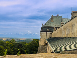 Visiting a castle on a cloudy day. Visitors walk by an old castle with green trees and blue skies in the background. The scene captures history and nature. © Daniil