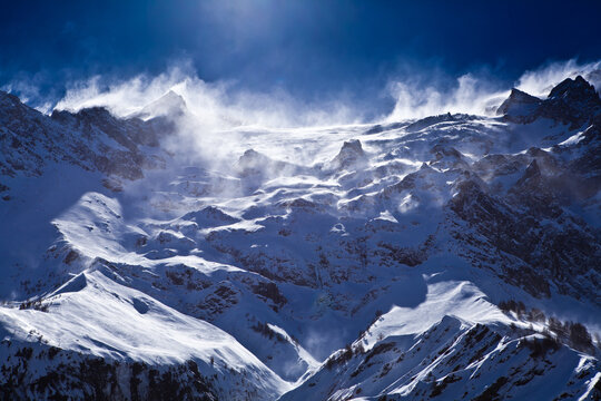 Strong wind blowing snow from high alpine mountain peak at winter
