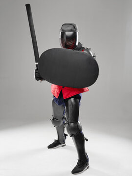 HEMA fighter with shield raised and padded sword extended in defensive posture.
