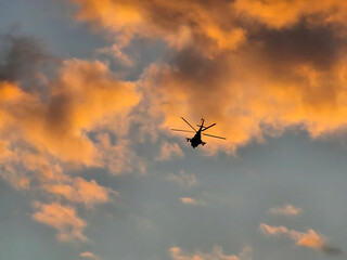 Helicopter Silhouette Flying Against Dramatic Orange Sunset Clouds, Atmospheric Aviation and Travel Photography Background © Siam