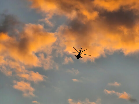 Helicopter Silhouette Flying Against Dramatic Orange Sunset Clouds, Atmospheric Aviation and Travel Photography Background