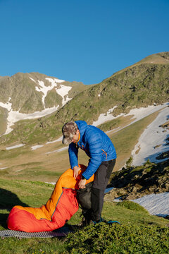 UGC Man packing orange sleeping bag at sunrise in the Pyrenees