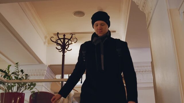 Close up of man in dark clothing descending indoor stairs with steady movement. subject interacts minimally maintaining neutral expression while holding stair railing for support. Background