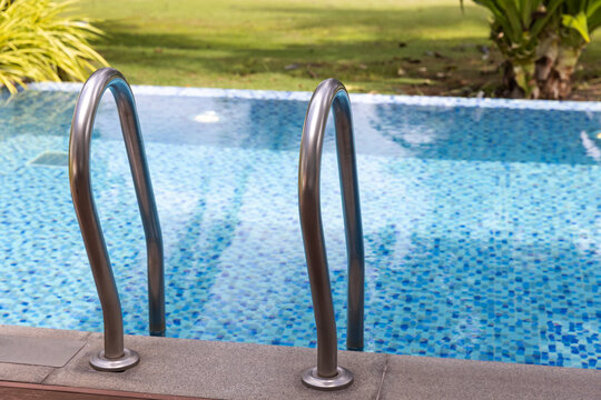 Outdoor mosaic-tiled swimming pool with a stainless steel ladder at the pool edge, calm blue water and a grassy backyard creating a relaxing, summery atmosphere for leisure and recreation