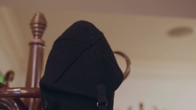 Person hangs black hat on one of hooks in indoor setting. background features soft lighting and neutral tones with no other objects or actions visible