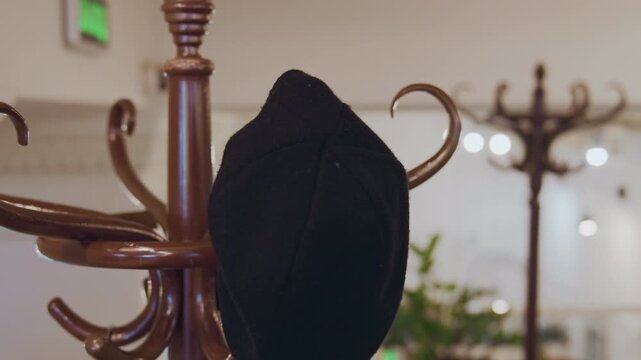 Close up of person hanging and adjusting black hat on ornate brown coat rack in soft indoor lighting. hand briefly interacts with fabric ensuring proper placement among other hooks