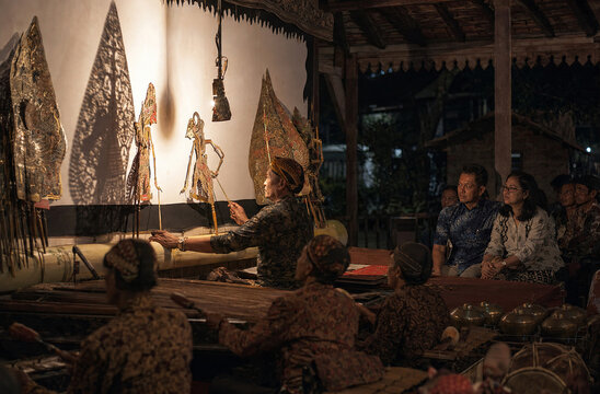 An ancient tradition comes alive as a puppeteer skillfully manipulates shadow puppets against a illuminated screen, captivating a rapt audience with a mesmerizing performance of cultural storytelling.