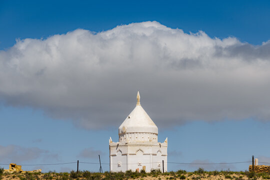 View of the white Karynzharyk mausoleum set against a bright blue sky with a large cloud in Karakiya District, Mangystau Region, Kazakhstan.