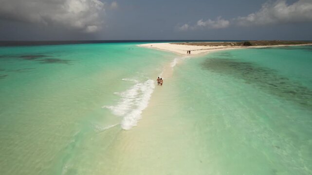 Aerial view of a pristine sandbar surrounded by turquoise waters in the Los Roques archipelago with people walking in the shallows in Los Roques, Dependencias Federale, Venezuela.